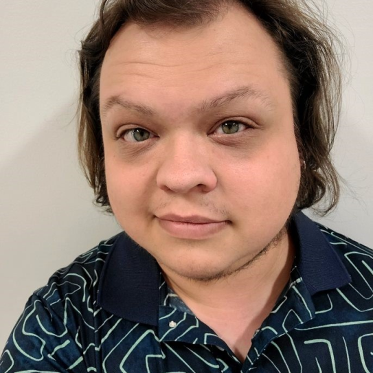 a portrait photo of a white individual with medium length brown hair and wearing a dark blue polo shirt taken from the chest up standing in front of a light gray background