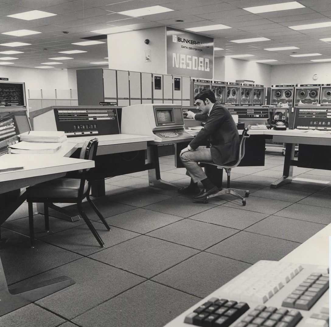 Man sittung at large computer terminal under NASDAQ sign